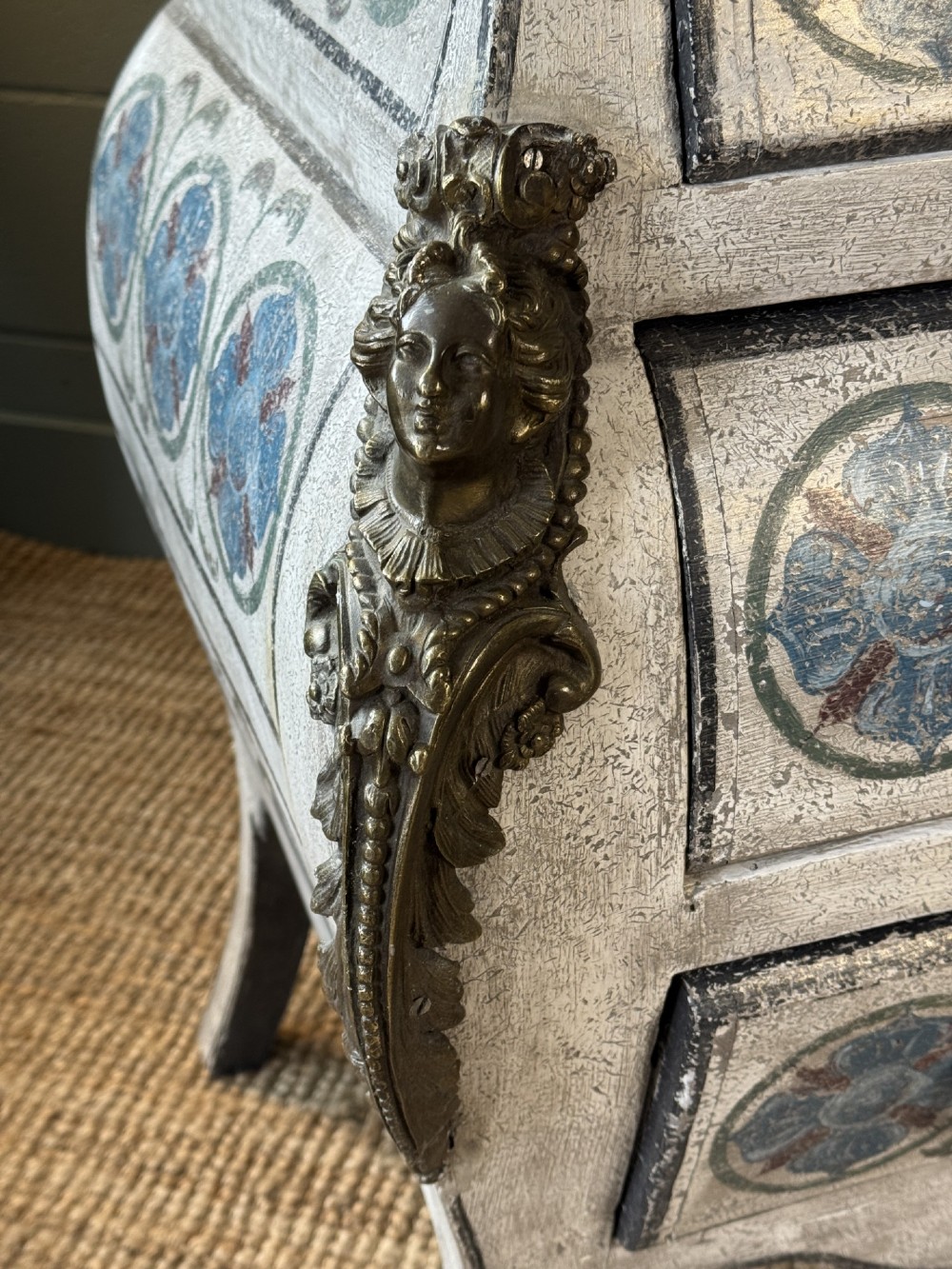 A nineteenth-century French bombee chest of drawers featuring a later hand-painted pattern, a dark marble top, and ornate gilt bronze mounts. View IV