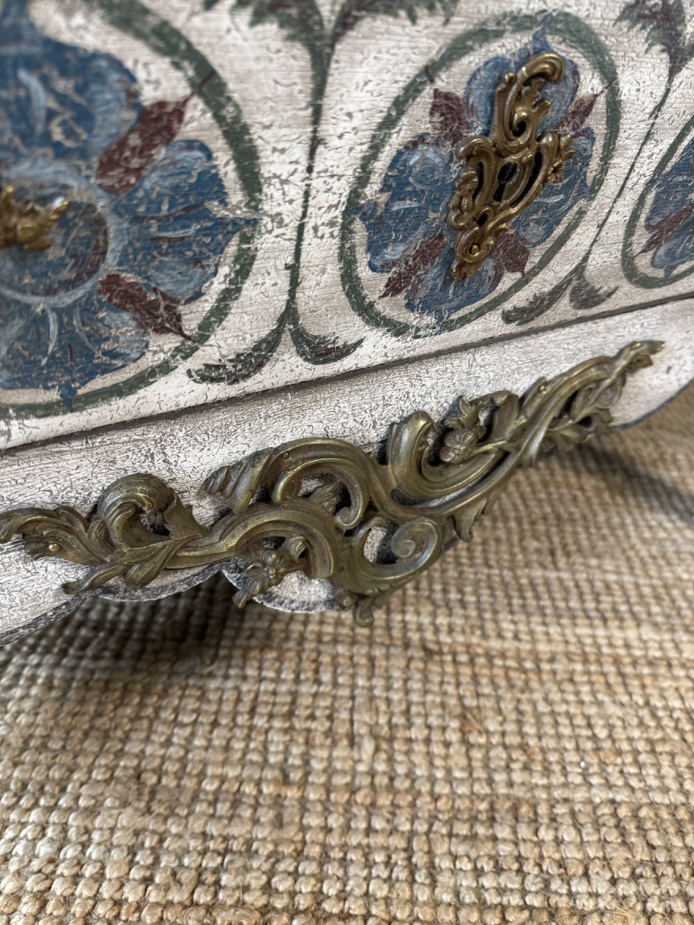 A nineteenth-century French bombee chest of drawers featuring a later hand-painted pattern, a dark marble top, and ornate gilt bronze mounts. View V