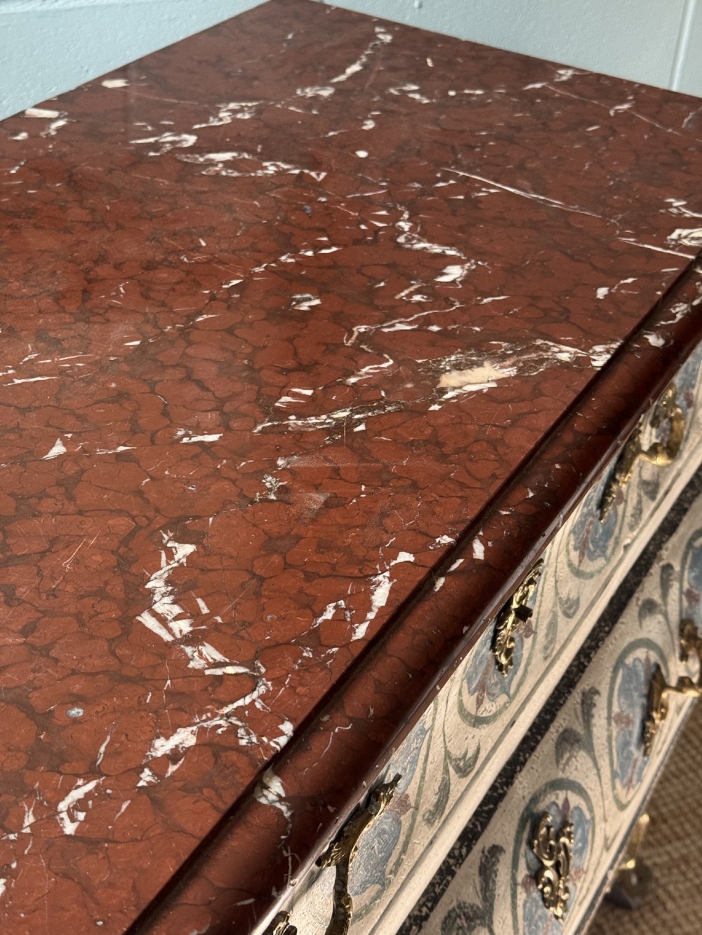 A nineteenth-century French bombee chest of drawers featuring a later hand-painted pattern, a dark marble top, and ornate gilt bronze mounts. View VI