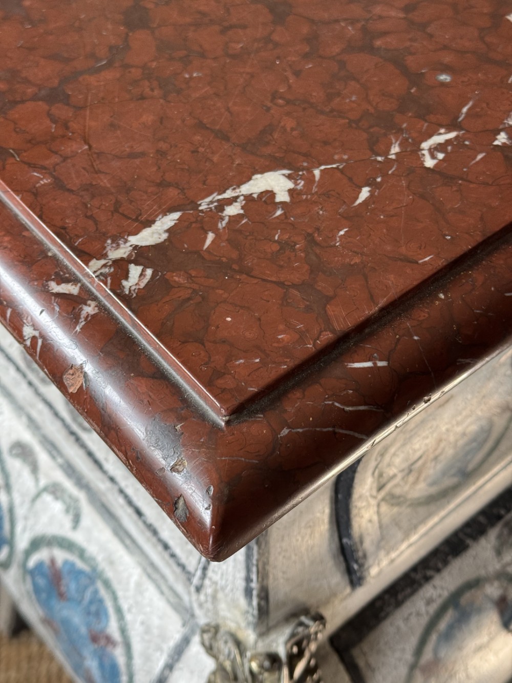 A nineteenth-century French bombee chest of drawers featuring a later hand-painted pattern, a dark marble top, and ornate gilt bronze mounts. View VII