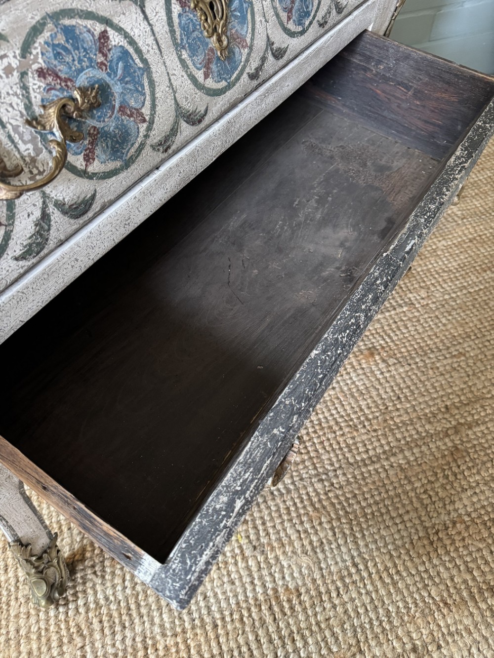 A nineteenth-century French bombee chest of drawers featuring a later hand-painted pattern, a dark marble top, and ornate gilt bronze mounts. View XII
