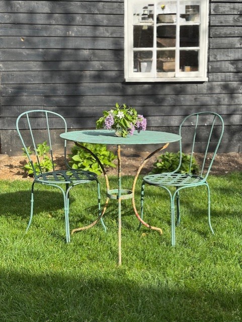 A weathered green painted wrought iron bistro set featuring a round pedestal table and two hoop-back chairs with lattice seats.