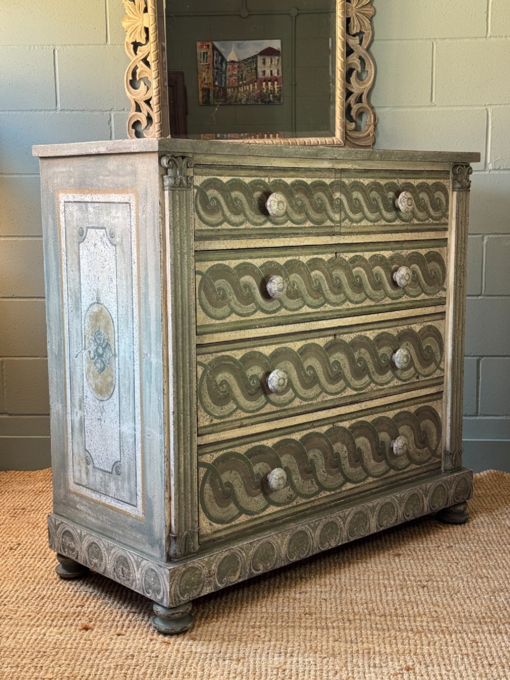 A grey-green hand-painted French Empire chest of drawers featuring guilloche drawer decoration, fluted pilasters, and side cartouche panels.
