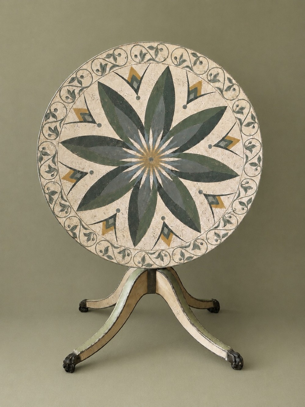 A circular Victorian tilt-top table featuring hand-painted geometric and botanical foliage patterns in green and yellow on a cream ground, resting on a tripod base with brass claw feet. View III