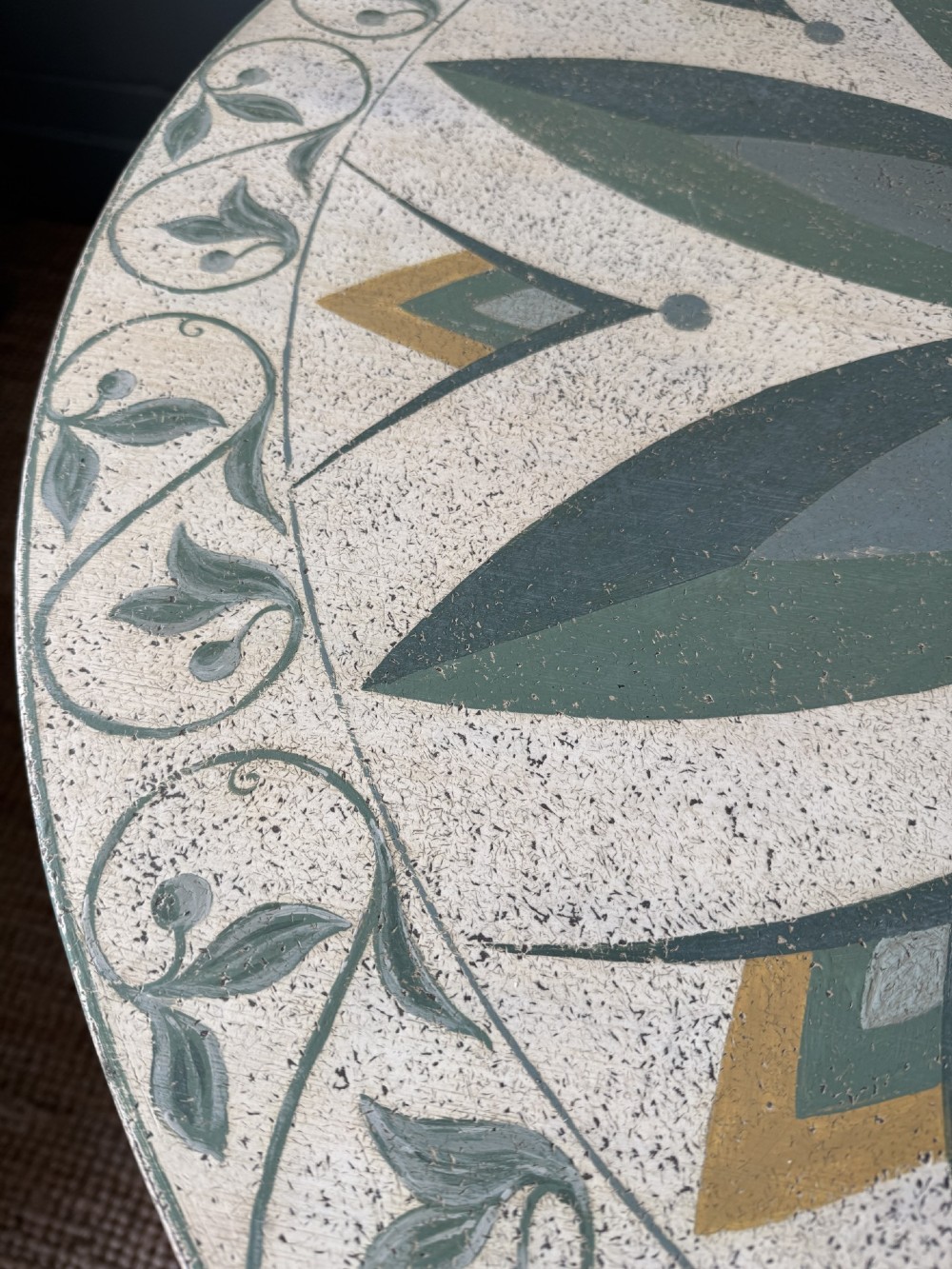 A circular Victorian tilt-top table featuring hand-painted geometric and botanical foliage patterns in green and yellow on a cream ground, resting on a tripod base with brass claw feet. View VI