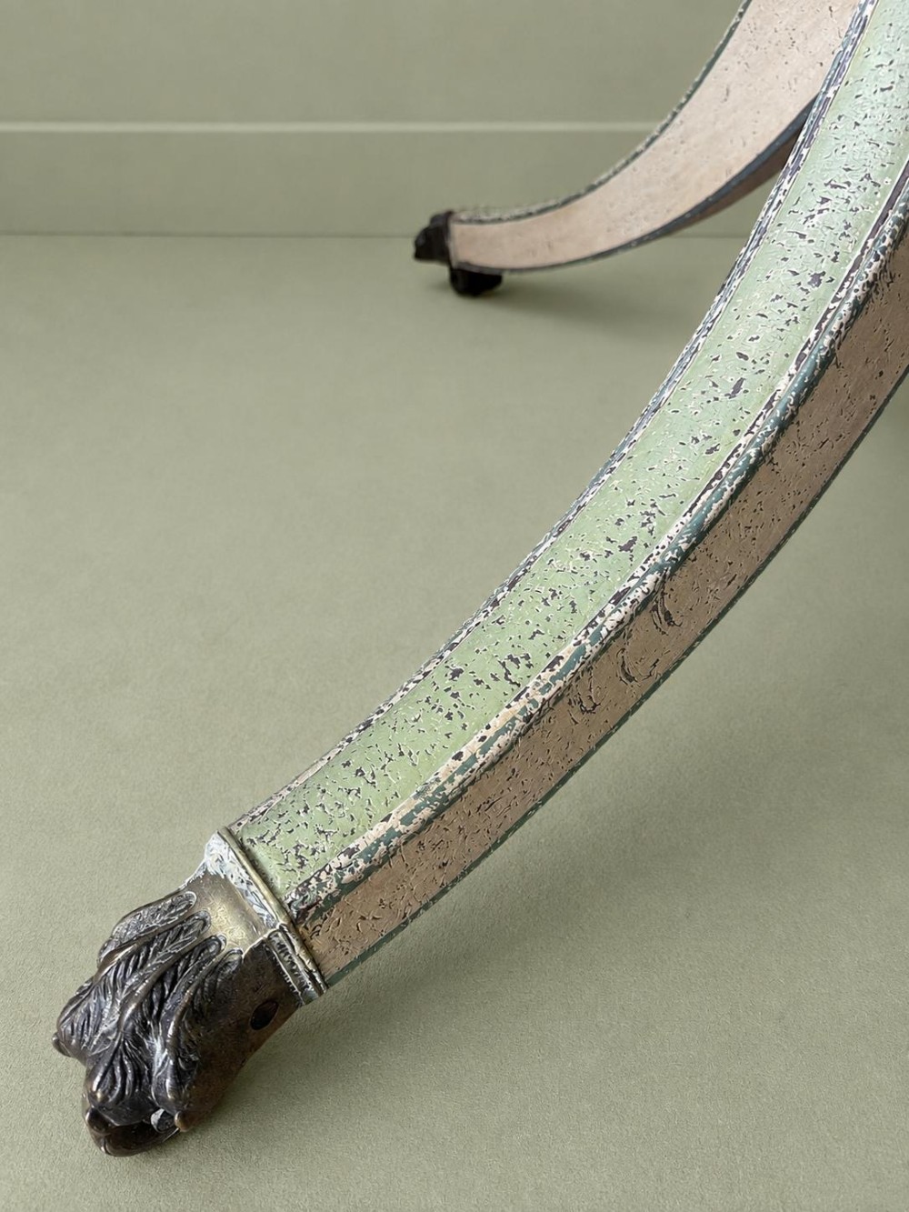 A circular Victorian tilt-top table featuring hand-painted geometric and botanical foliage patterns in green and yellow on a cream ground, resting on a tripod base with brass claw feet. View VII