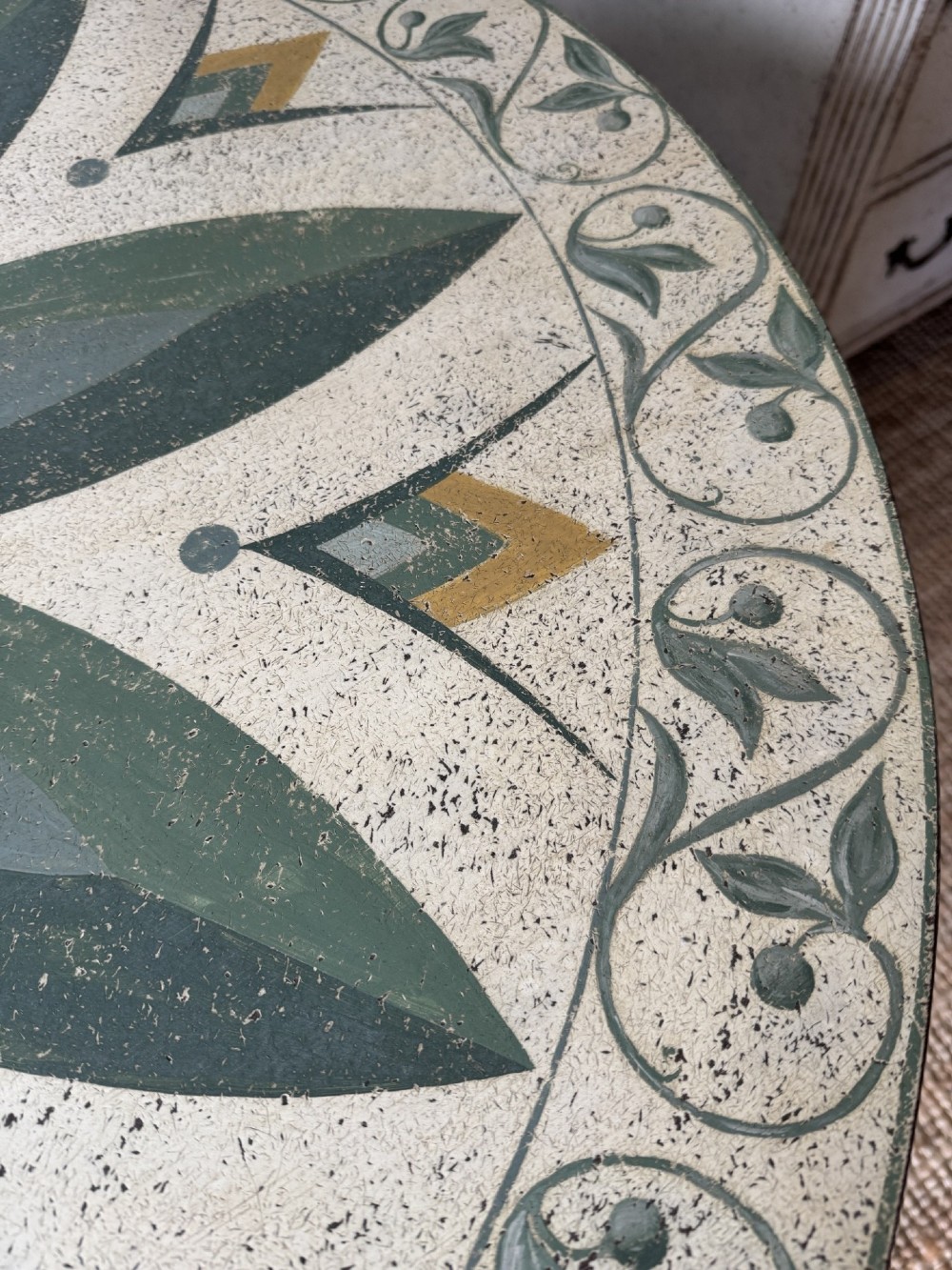 A circular Victorian tilt-top table featuring hand-painted geometric and botanical foliage patterns in green and yellow on a cream ground, resting on a tripod base with brass claw feet. View VIII