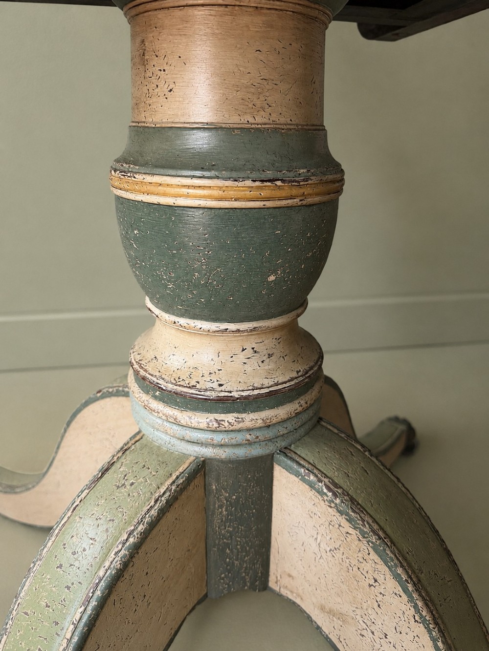 A circular Victorian tilt-top table featuring hand-painted geometric and botanical foliage patterns in green and yellow on a cream ground, resting on a tripod base with brass claw feet. View X