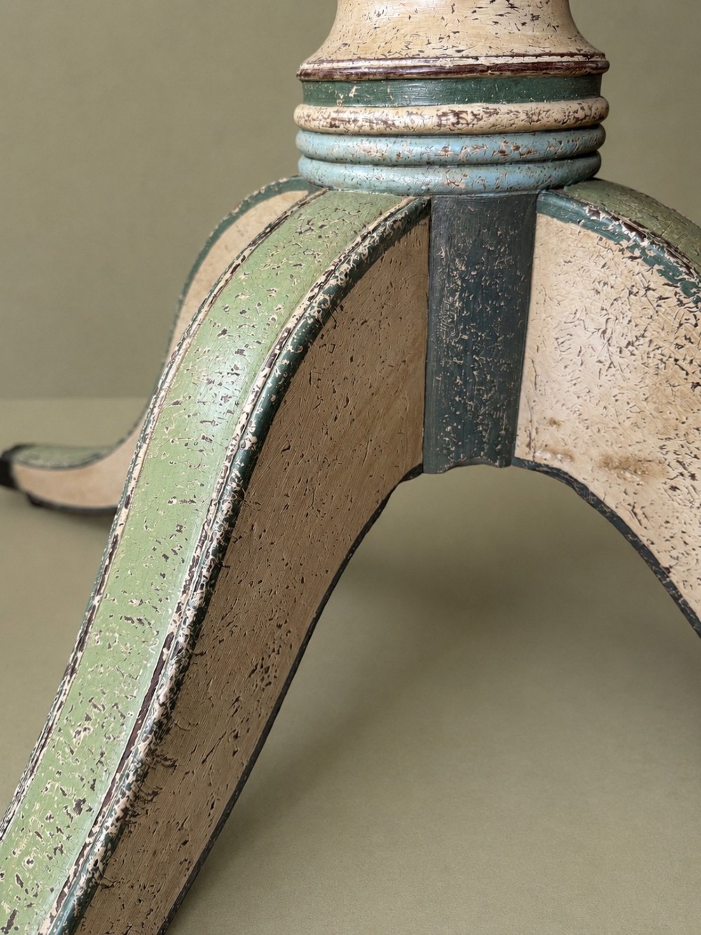 A circular Victorian tilt-top table featuring hand-painted geometric and botanical foliage patterns in green and yellow on a cream ground, resting on a tripod base with brass claw feet. View XI