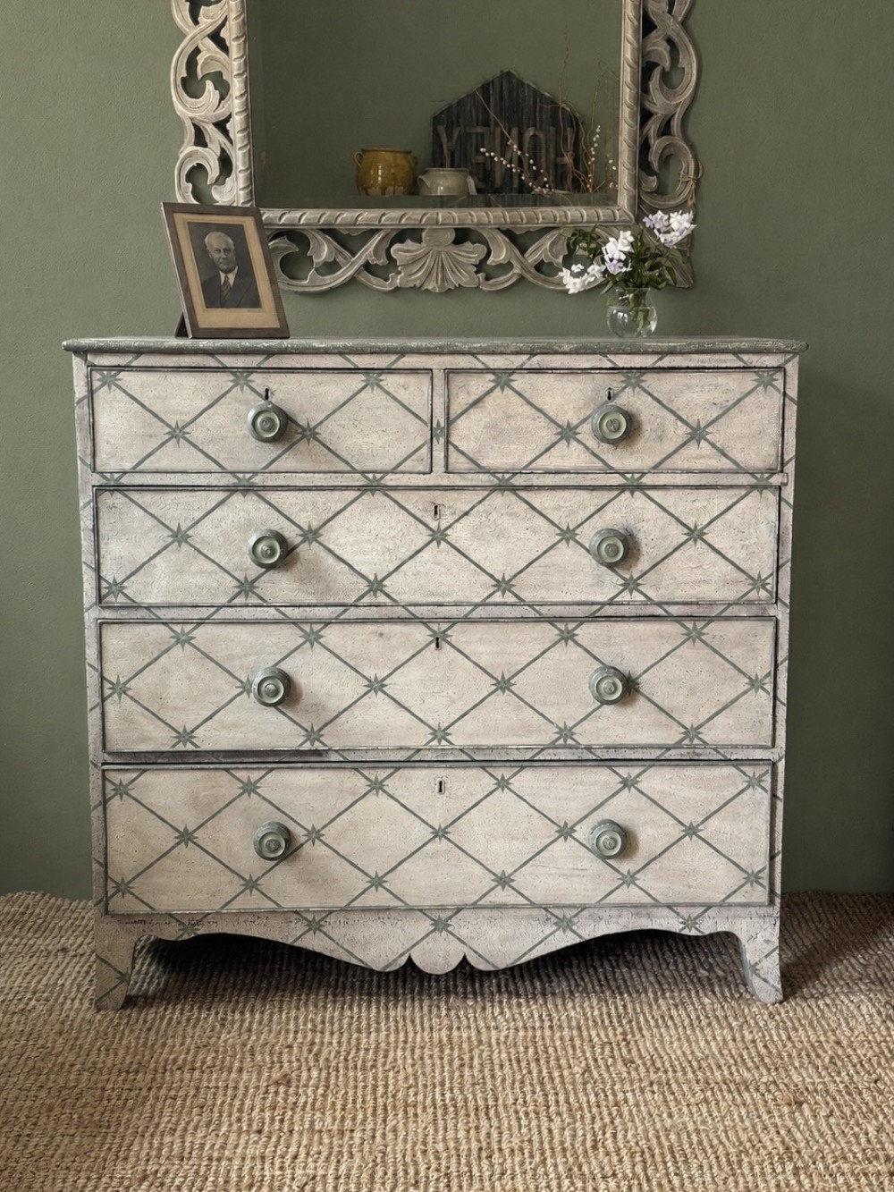 A Victorian painted wooden chest of drawers featuring a grey geometric star trellis pattern over an off-white finish, fitted with turned wooden knobs and a shaped lower apron.