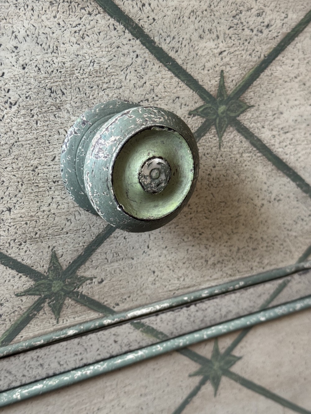 A Victorian painted wooden chest of drawers featuring a grey geometric star trellis pattern over an off-white finish, fitted with turned wooden knobs and a shaped lower apron. View II