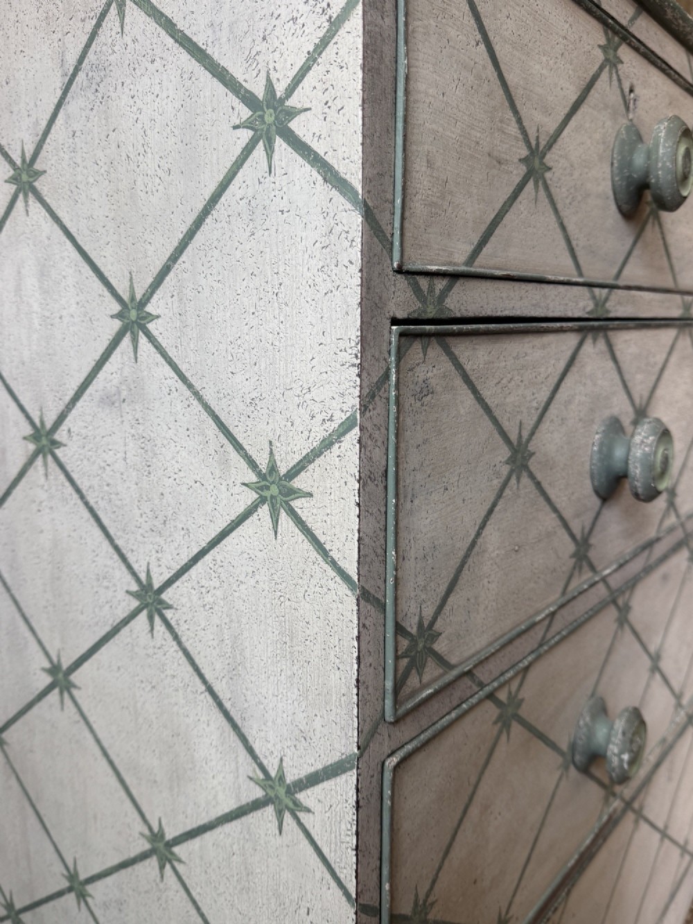 A Victorian painted wooden chest of drawers featuring a grey geometric star trellis pattern over an off-white finish, fitted with turned wooden knobs and a shaped lower apron. View III