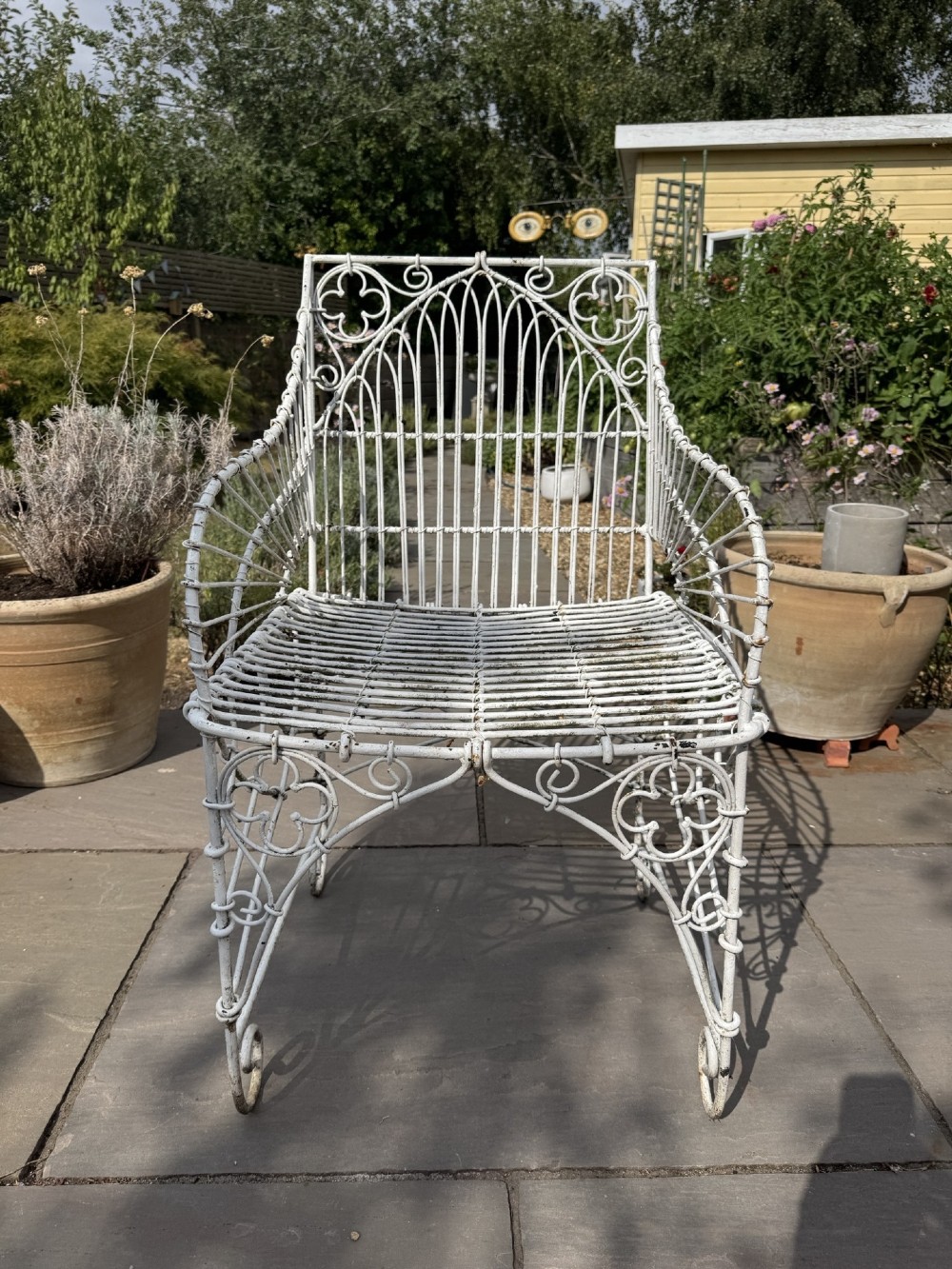 A white wrought iron garden set featuring a circular wirework table and four matching armchairs with pink and white striped cushions. View V