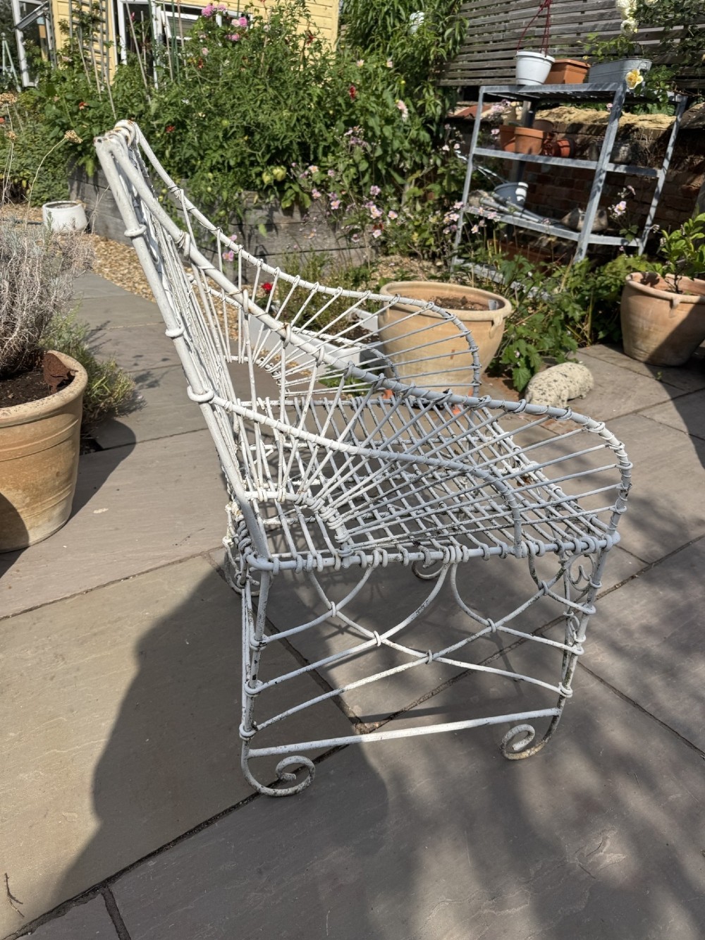 A white wrought iron garden set featuring a circular wirework table and four matching armchairs with pink and white striped cushions. View VI