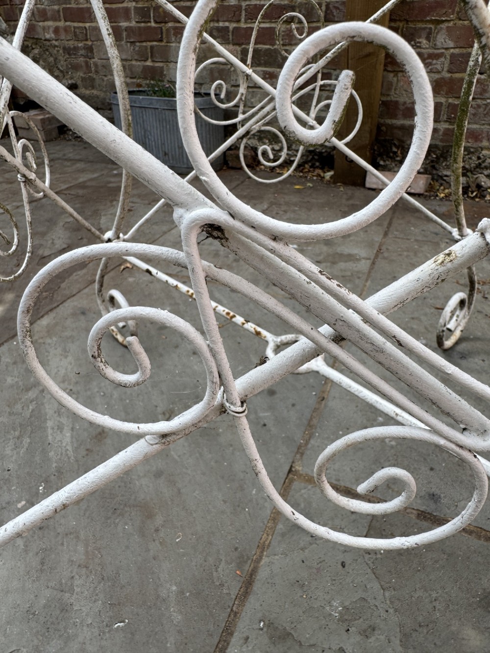 A white wrought iron garden set featuring a circular wirework table and four matching armchairs with pink and white striped cushions. View VII