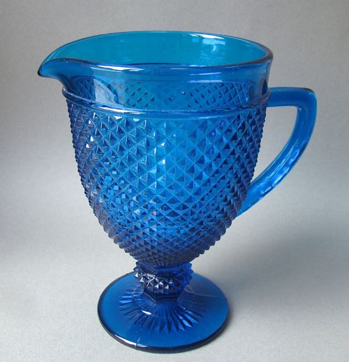 fig 1. A cobalt blue Victorian pressed glass water jug featuring a diamond pattern body, moulded handle, smooth rim, and circular pedestal foot.