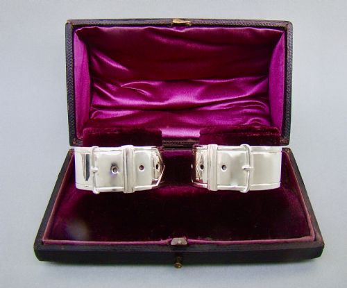 fig 1. A pair of Victorian silver-plated napkin rings designed to resemble buckled belts, resting inside a velvet-lined presentation box.