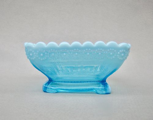 fig 1. A square blue opalescent pressed glass bowl featuring a scalloped rim and moulded daisy pattern on a footed base.
