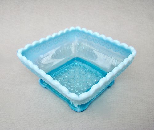 fig 2. A square blue opalescent pressed glass bowl featuring a scalloped rim and moulded daisy pattern on a footed base.