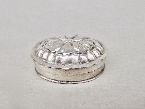 fig 1. A small round Dutch silver pill box featuring a scalloped rim and an embossed floral repousse lid.