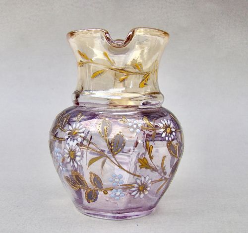 fig 1. A late Victorian glass cream jug featuring purple and clear iridescent glass decorated with hand-painted white and gold enamelled floral motifs and an applied clear handle.