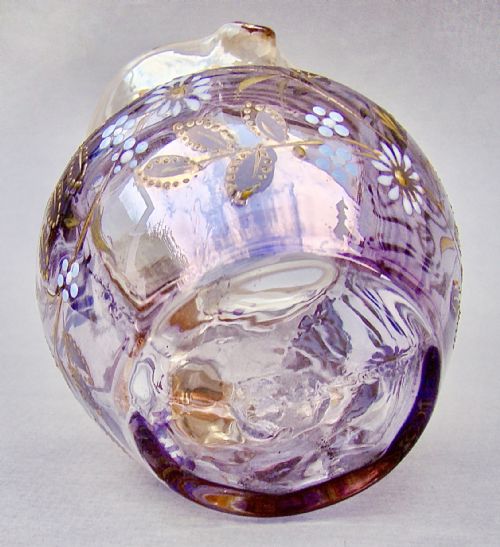 fig 2. A late Victorian glass cream jug featuring purple and clear iridescent glass decorated with hand-painted white and gold enamelled floral motifs and an applied clear handle.