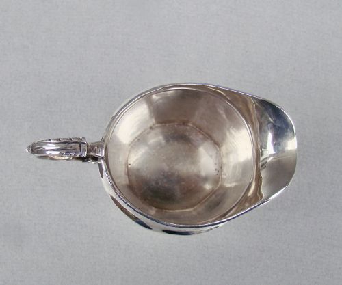 fig 2. A polished George V sterling silver cream jug featuring a faceted body, C-scroll handle, and stamped English hallmarks near the gadrooned rim.