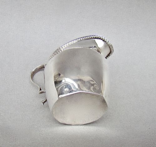 fig 3. A polished George V sterling silver cream jug featuring a faceted body, C-scroll handle, and stamped English hallmarks near the gadrooned rim.