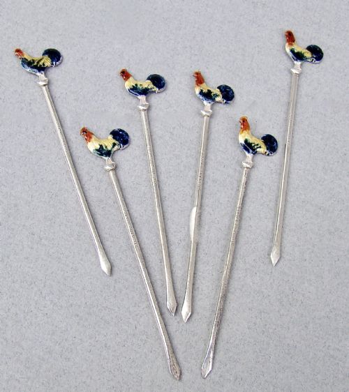 fig 1. A cased set of six sterling silver cocktail sticks featuring colourful enamelled cockerel finials arranged inside a fitted cream-lined presentation box.