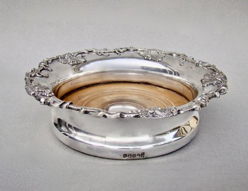 fig 1. A circular William IV Old Sheffield Plate wine coaster featuring a turned wooden insert, central silver boss, and a chased border decorated with grapevines and leaves.