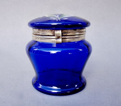 fig 1. A deep cobalt blue glass dressing table jar featuring hand-painted white daisy enamel decoration and a hinged metal rim.