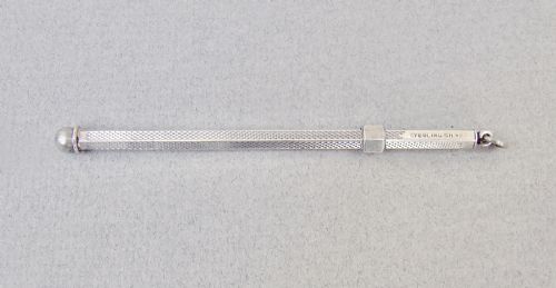 fig 2. An Art Deco sterling silver swizzle stick featuring an engine-turned cylindrical handle, a suspension ring, and extendable wire prongs at the top.