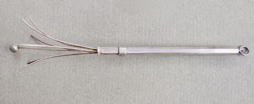 fig 1. An Art Deco sterling silver swizzle stick featuring an engine-turned cylindrical handle, a suspension ring, and extendable wire prongs at the top.