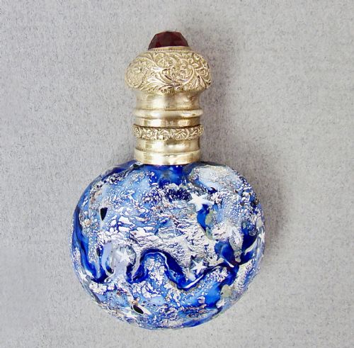 fig 1. A round cobalt blue Murano glass scent bottle featuring swirl patterns, silver leaf inclusions, star murrine, and an embossed silver-gilt cap set with a red gemstone.