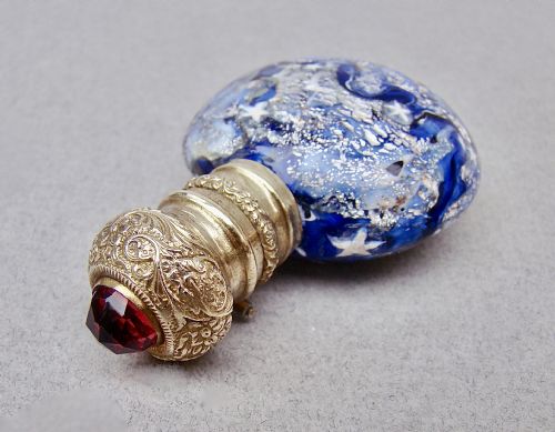 fig 2. A round cobalt blue Murano glass scent bottle featuring swirl patterns, silver leaf inclusions, star murrine, and an embossed silver-gilt cap set with a red gemstone.