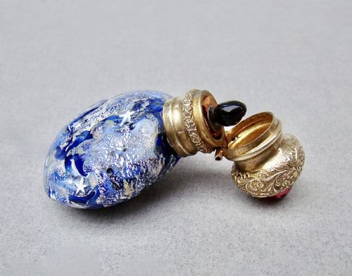 fig 3. A round cobalt blue Murano glass scent bottle featuring swirl patterns, silver leaf inclusions, star murrine, and an embossed silver-gilt cap set with a red gemstone.