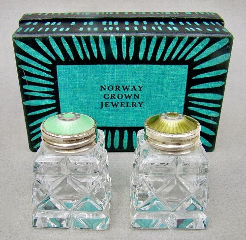 fig 1. A pair of Art Deco cut glass salt shakers featuring green guilloche enamel and silver tops, shown in front of their fitted presentation box.