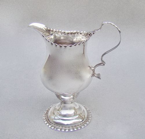 fig 1. A Georgian sterling silver cream jug featuring a baluster shape, beaded rim, pedestal base, and engraved initials, assayed in London in 1777.