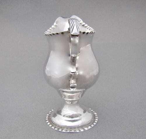 fig 2. A Georgian sterling silver cream jug featuring a baluster shape, beaded rim, pedestal base, and engraved initials, assayed in London in 1777.