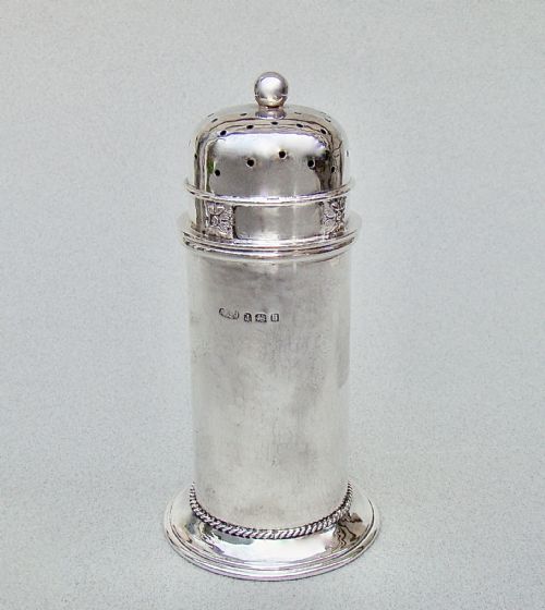 fig 1. A cylindrical sterling silver sugar caster featuring a domed perforated lid, floral band motif, rope twist base, and visible English hallmarks.