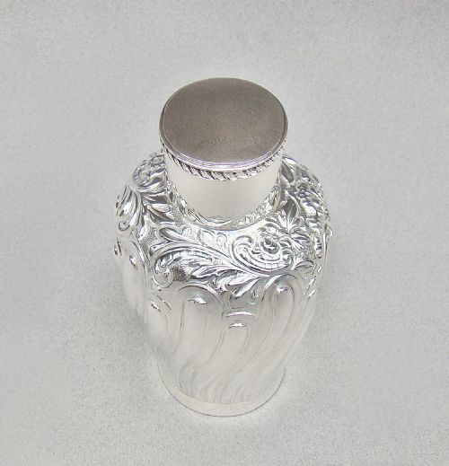 fig 1. An Edwardian sterling silver tea caddy featuring repousse floral scroll decoration, a gadrooned rim lid, and British hallmarks stamped on the neck.
