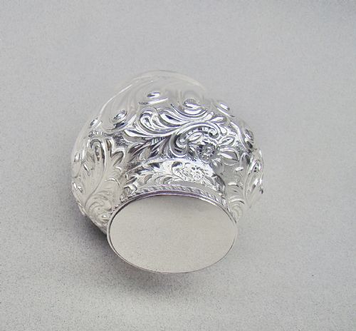 fig 2. An Edwardian sterling silver tea caddy featuring repousse floral scroll decoration, a gadrooned rim lid, and British hallmarks stamped on the neck.