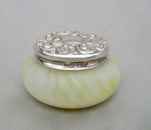 fig 1. A circular cream-coloured satin glass trinket box featuring a sterling silver lid embossed with scrollwork and floral details.