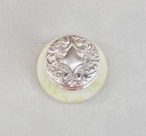fig 2. A circular cream-coloured satin glass trinket box featuring a sterling silver lid embossed with scrollwork and floral details.