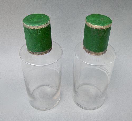 fig 2. A pair of clear glass 19th-century apothecary jars featuring white etched Latin labels and cylindrical green painted stoppers with metallic rims.