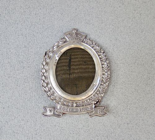 fig 1. A miniature oval sterling silver photo frame featuring a crowned crest, a laurel leaf frame, and a commemorative banner.