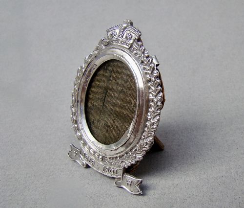 fig 2. A miniature oval sterling silver photo frame featuring a crowned crest, a laurel leaf frame, and a commemorative banner.