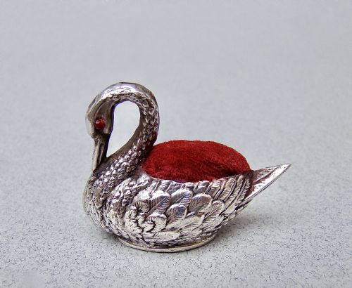 fig 1. An Edwardian sterling silver swan pin cushion featuring chased feather details, a red glass eye, and a red velvet cushion insert.