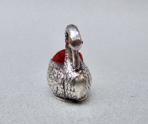 fig 2. An Edwardian sterling silver swan pin cushion featuring chased feather details, a red glass eye, and a red velvet cushion insert.