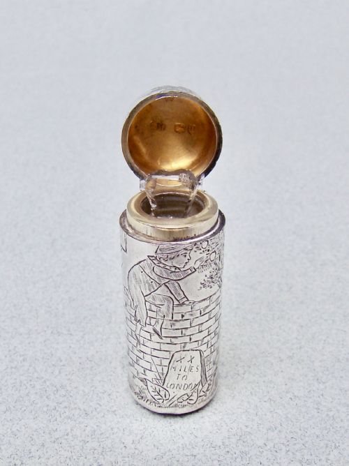 fig 3. A cylindrical Victorian sterling silver scent bottle decorated with an engraved illustration of a child on a brick wall near a milestone.